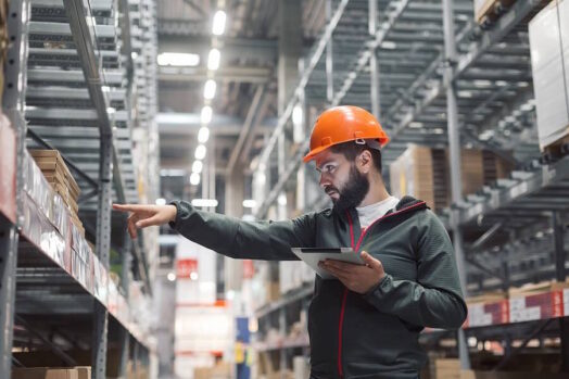 Man checking inventory in a large warehouse with his iPad in hand